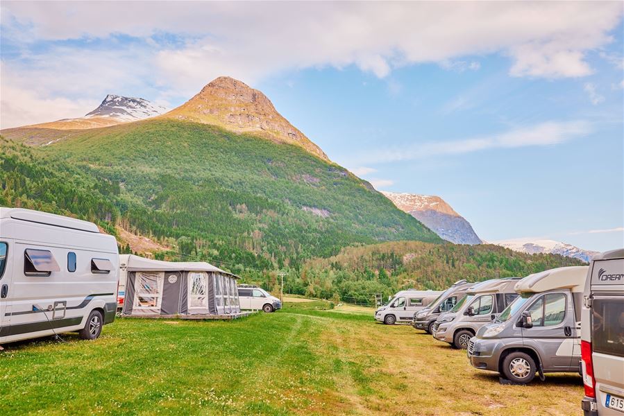 Rekkje bubilar på grasmark ved camping, med telt og grøne fjellsider under blå himmel med skyer..