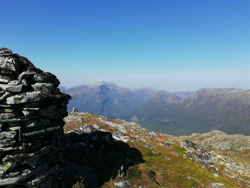 Steinvarde på Helsethornet, utsikt over fjell og dalar under klar blå himmel..