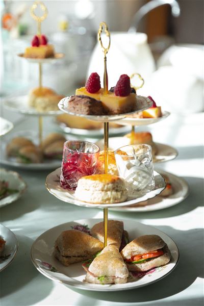 Eit etasjefat med små smørbrød, scones, syltetøy og kaker med bringebær, i mjukt dagslys..