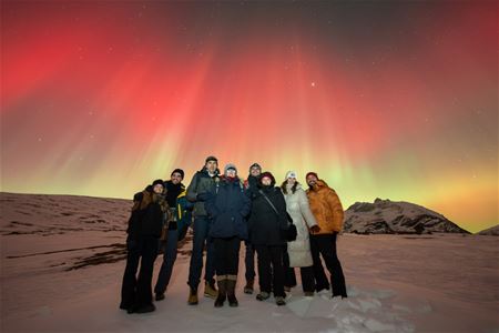 Rødt nordlys knitrer bak en gruppe med gjester