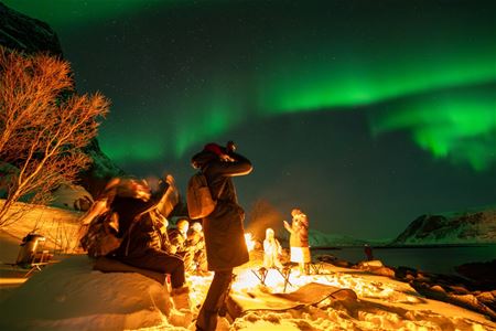 En gjest tar bilde av nordlyset ved siden av bålet