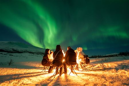 Gjester samler seg rundt bålet mens nordlyset danser i bakgrunnen