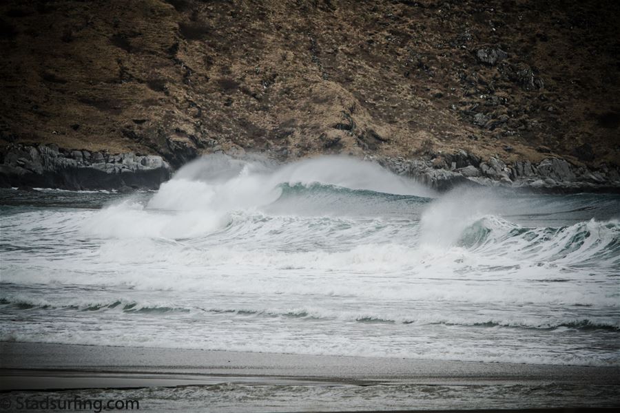 Kraftige havbølgjer i Ervik bryt og skummar inn mot ei steinete kystline med bratt, brun åsside i bakgrunnen..