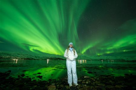 A guest poses in front of a Northern Lights show covering the whole sky