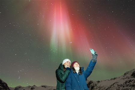 A couple takes a selfie with red Aurora in the background