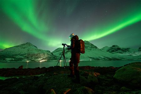 A photographer points the camera up at the Northern Lights, which creates an arch overhead