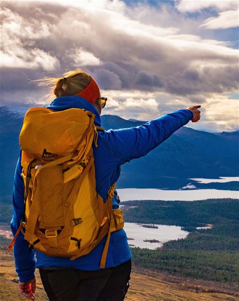 Person med tursekk peker utover et fjellandskap med innsjøer.