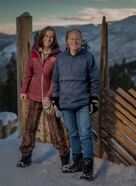 To personer står ved et gjerde i vinterfjellet.