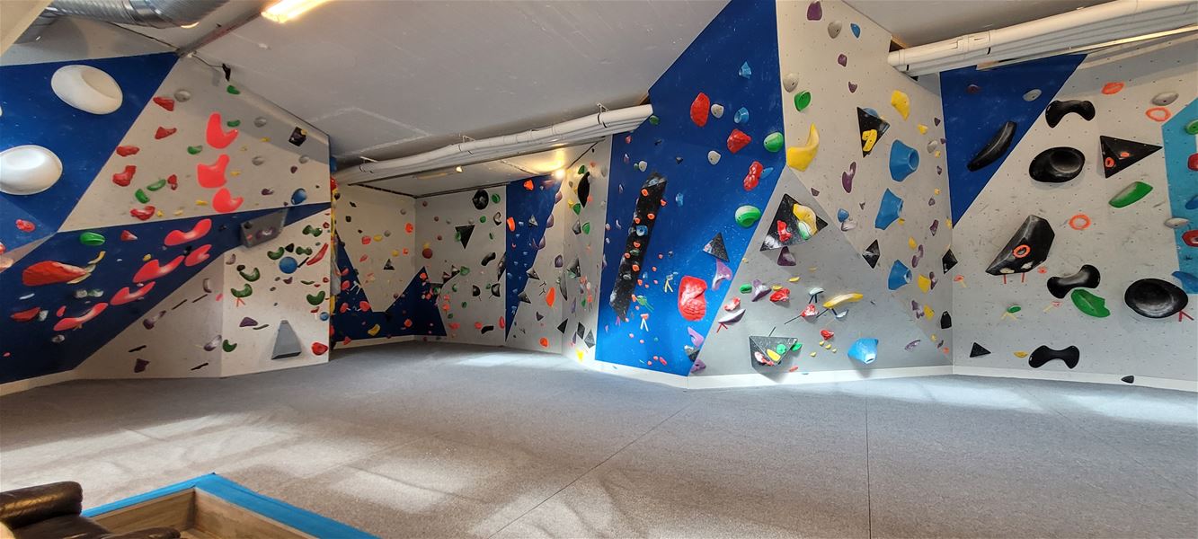 Empty indoor bouldering gym with blue and gray climbing walls covered in colorful holds and thick padded flooring..
