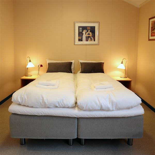 Two twin beds with white duvets, folded towels, bedside lamps, and framed art on a beige wall..