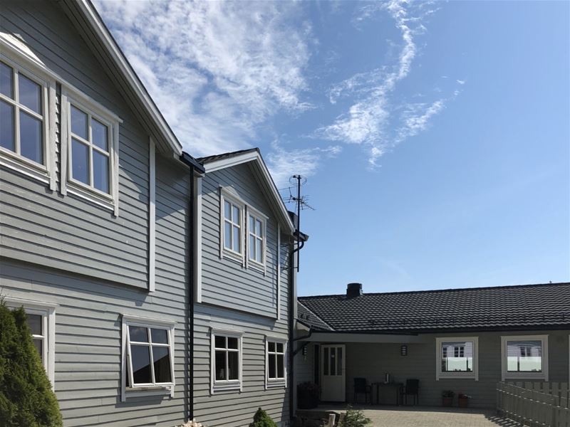 Exterior of a gray wooden house with white-trim windows, a courtyard, and blue sky with wispy clouds..