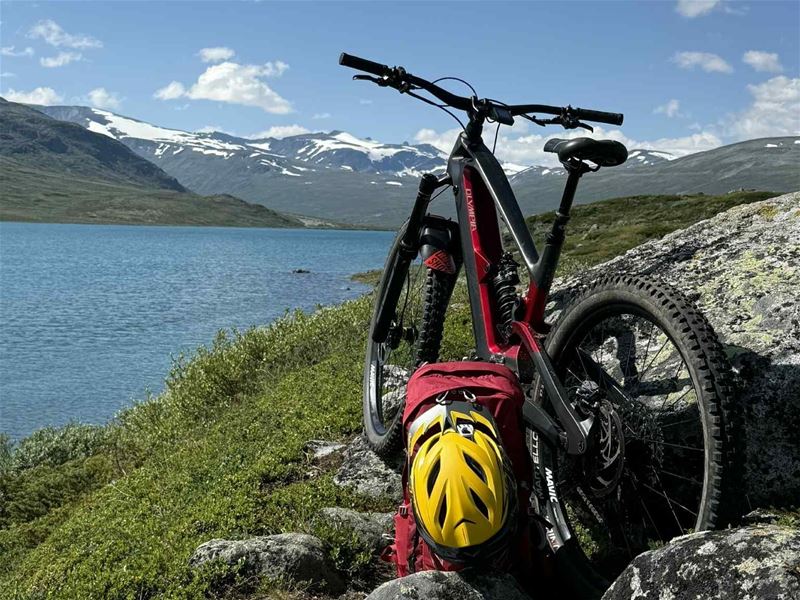 Mountain bike and helmet placed by a mountain lake with mountains in the background.