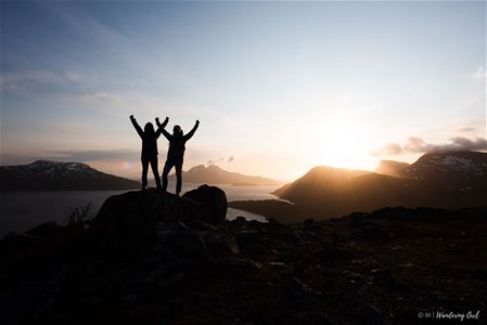 To personer som løfter hendene i været foran midnattssola