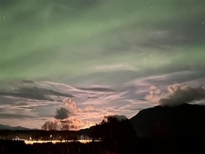 Nordlys skinner over fjell og tynne skyer