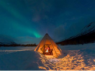 Et telt med gjester inni og nordlys over i et vinterlandskap