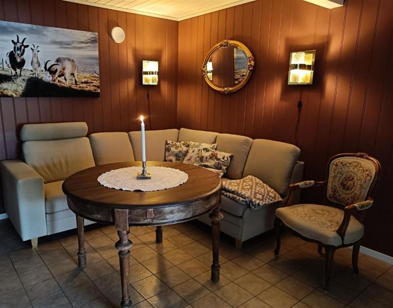 Orheimstunet i Nordfjord - Koseleg hjørnestove med hjørnesofa, rundt trebord med tent lys og duk, vegglamper, bilete og spegel..