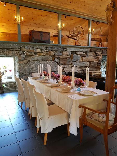 Orheimstunet i Nordfjord - Langt bord dekka med kvit duk, servise og blomster i ei rustikk stove med steinvegg og treloft..