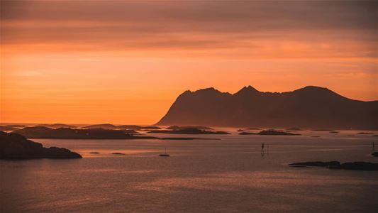 Kystlandskap med fjell i bakgrunnen under midnattssola