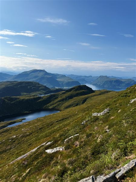 Tarvaldseggja - Topptur Ved Storhavet i Selje –Vidt landskap med grøne fjellryggar, vatn i dalen og fjord i bakgrunnen under klar blå himmel..