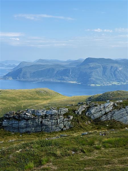 Tarvaldseggja - Topptur Ved Storhavet i Selje –Utsyn frå grønt fjellterreng med steinrøys i forgrunnen, blå fjord og fjellryggar under lys himmel..