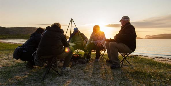 En gruppe gjester som sitter rundt et bål ved fjæra