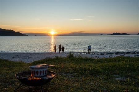Bål ved fjæra med gjester som ser på solnedgangen