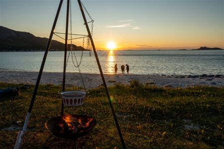 Bål på stranden med gjester som ser på solnedgangen