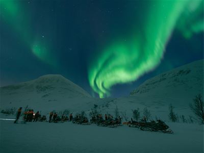 Snøskutere står klar foran fjell og aurora