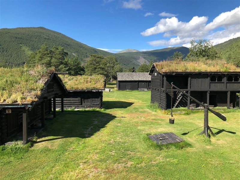 Historic wooden buildings at Jørundgard surrounded by green countryside and mountains.