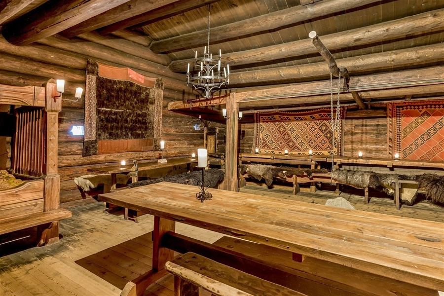  Interior of a longhouse with long table, wooden benches, and traditional decorations.