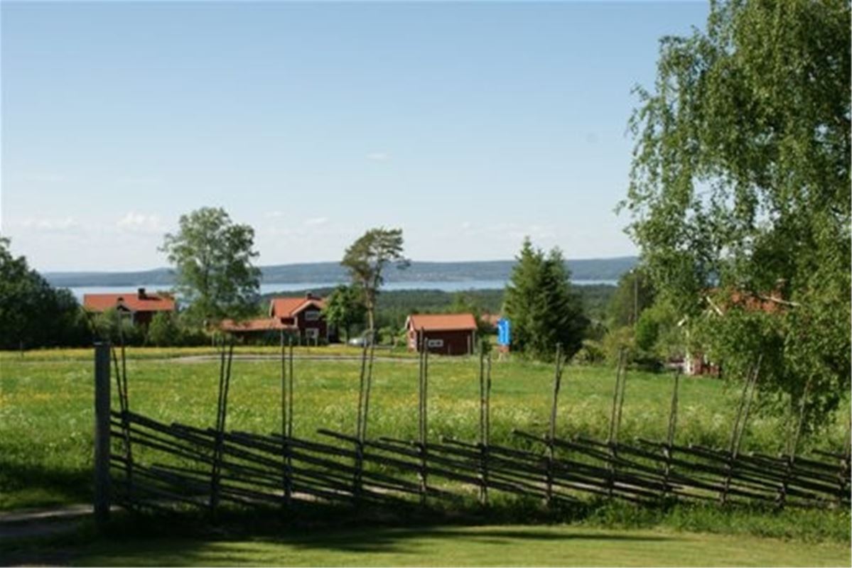 View over fields and dalecarlian fence with cottages and the lake further away.