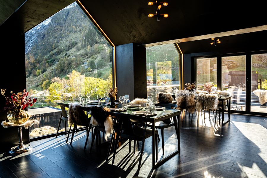Moderne spiserom med mørke vegger, bord dekka med glas og servise, og store vindauge mot fjellandskap på Sølvene Gard Restaurant i Kandal i Gloppen..
