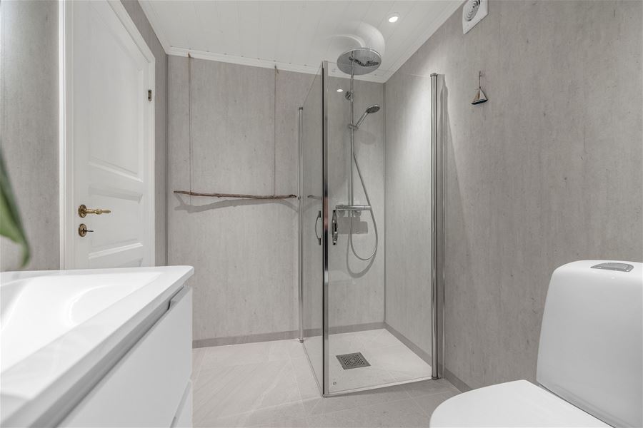 Modern gray bathroom with glass shower enclosure, rainfall showerhead, white vanity, and toilet under recessed lights at the Seahouse at Hornelen Panorama in Bremanger..