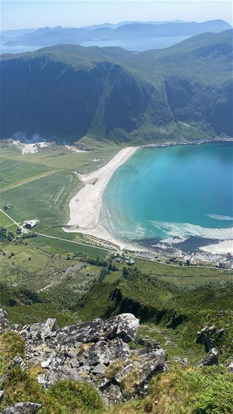 Panoramautsikt frå fjell mot ei turkis bukt med kvit sandstrand, grøne marker og bratte fjellsider i bakgrunnen i Hoddevik i Nordfjord..