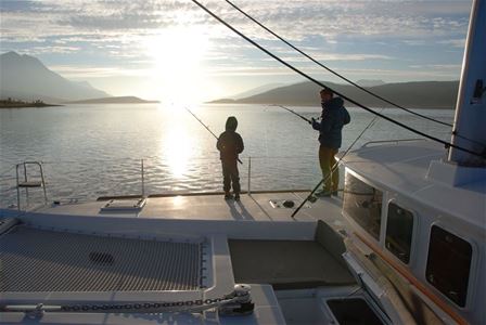 Two people fishing from a boat with the sunset in the background