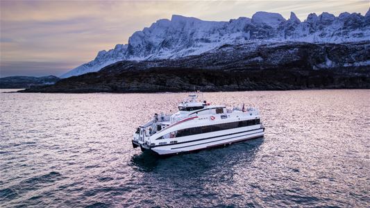 Båten i sjøen med vinterlandskap i bakgrunnen