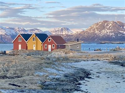Three buildings by the sea with mountains in the background