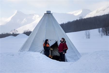 Two guests peep into a small traditional Sami lavvo