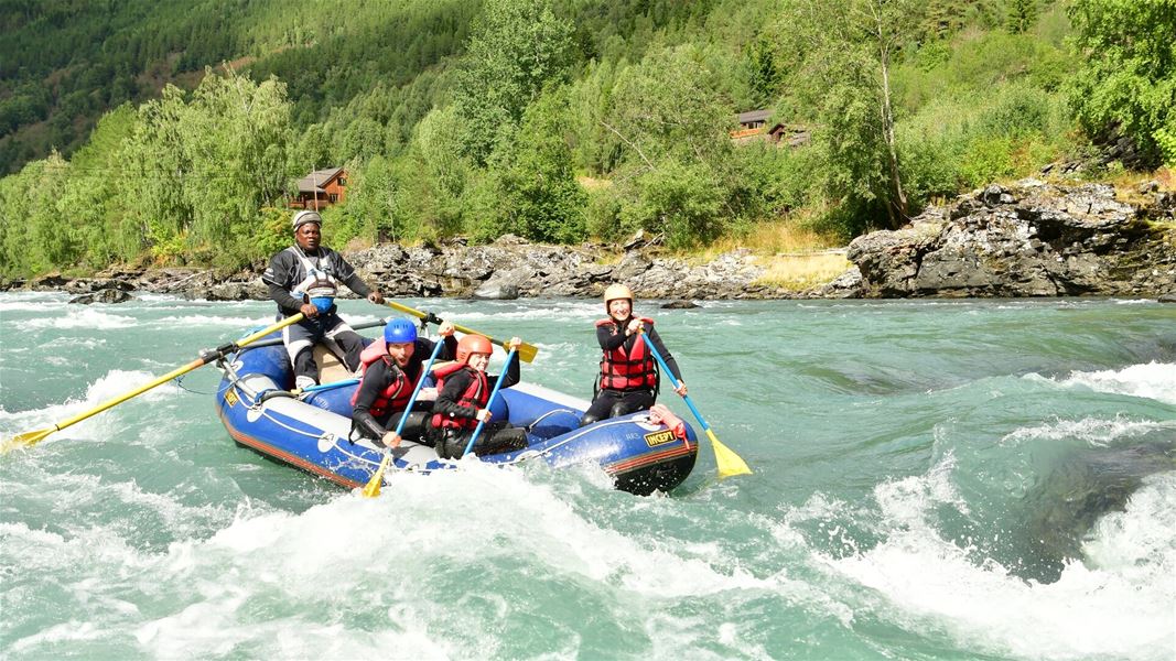 Rafting boat in whitewater rapids surrounded by mountains and forest.