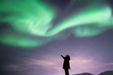 Guest pointing towards the Northern Lights in the snowy landscape