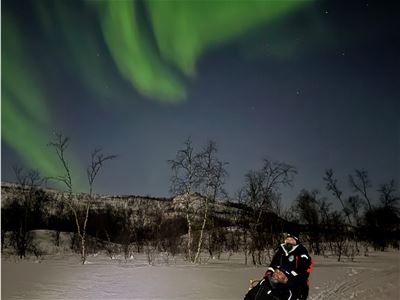 Hundefører under nordlyset i det snødekte landskapet i Skibotndalen
