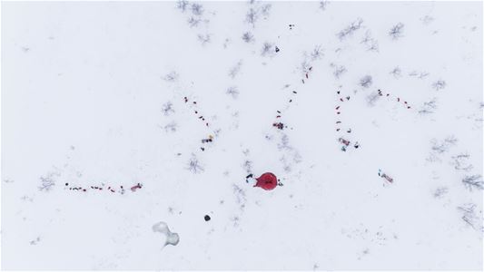 Dog teams and expedition tents seen from above in a snow-covered winter landscape.
