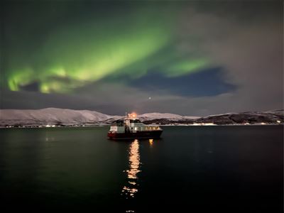 En båt på fjorden under nordlyset og den arktiske nattehimmelen.