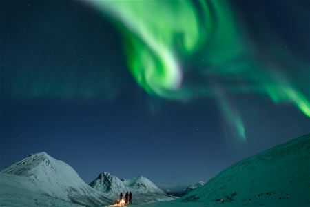 The Northern Lights illuminate the winter sky above snow-covered mountains outside Tromsø in Northern Norway.