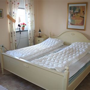 Dubbelsäng i en vit sängram och vita nattduksbord i ett rum med beige vägg.