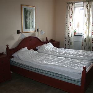 Double bed in a dark brown, wooden bed frame with matching chest of drawers besife. 
