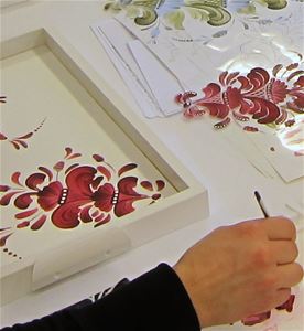 A white frame with a painting of a red flower, a hand holding a brush.