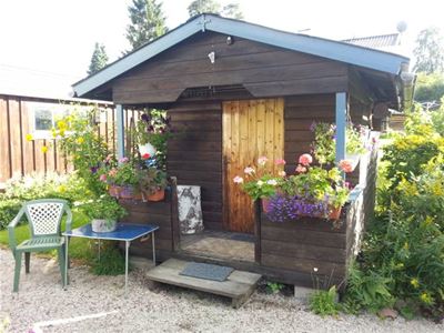 A small brown painted cabin with lots of flowers at the entrance.