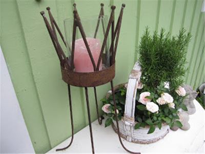 A candlestick in the shape of a crown, next to it a flower arrangement, in the background a light green wall.