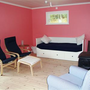 Rum med rosa väggar, vit dagbädd, två svarta fåtöljer med en fotpall. 